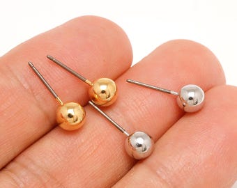 Op de afbeelding: Vier oorstekers. Twee zijn goudkleurig en twee zilverkleurig. Elke oorbel heeft een kleine, ronde bal aan een dunne pin. De oorbellen worden gepresenteerd tegen een lichte achtergrond.