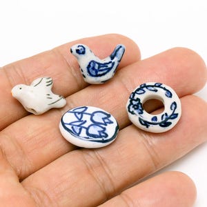 May include: Four ceramic beads with blue and white designs. The beads feature a bird, a flower, a wreath, and a plain bead.