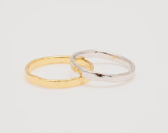 Puede incluir: Dos anillos, uno dorado y otro plateado, se muestran sobre un fondo blanco. Los anillos tienen un aspecto texturizado y martillado. El anillo dorado es de un amarillo brillante y brillante, mientras que el anillo plateado tiene un brillo metálico frío. Los anillos son bandas sencillas.
