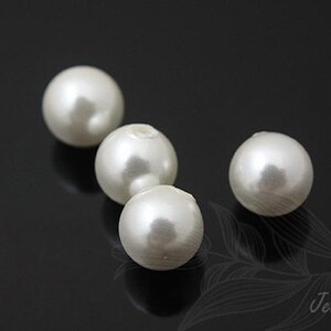 May include: Four white pearl beads on a black background. The beads are round and smooth.