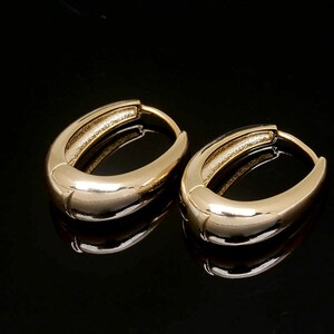 May include: A pair of gold oval hoop earrings. The earrings are smooth and shiny.