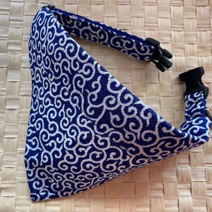 Puede incluir: Un pa&ntilde;uelo para perro con estampado azul y blanco con un collar ajustable a juego. El pa&ntilde;uelo presenta un dise&ntilde;o de remolino repetido. El collar tiene una hebilla de pl&aacute;stico negro y un lazo de metal para sujetar la correa. El fondo es una textura tejida.