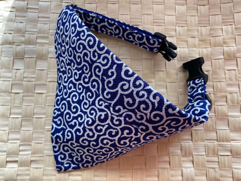 Puede incluir: Un pa&ntilde;uelo para perro con estampado azul y blanco con un collar ajustable a juego. El pa&ntilde;uelo presenta un dise&ntilde;o de remolino repetido. El collar tiene una hebilla de pl&aacute;stico negro y un lazo de metal para sujetar la correa. El fondo es una textura tejida.