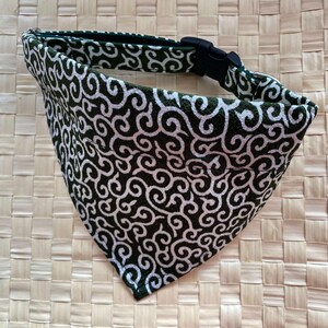 Puede incluir: Un pa&ntilde;uelo para perro con un dise&ntilde;o de remolino en blanco y negro. El pa&ntilde;uelo es triangular y tiene un collar negro ajustable con una hebilla de pl&aacute;stico negro. La tela tiene un borde verde oscuro.