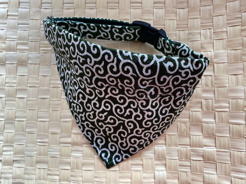Puede incluir: Un pa&ntilde;uelo para perro con un dise&ntilde;o de remolino en blanco y negro. El pa&ntilde;uelo es triangular y tiene un collar negro ajustable con una hebilla de pl&aacute;stico negro. La tela tiene un borde verde oscuro.