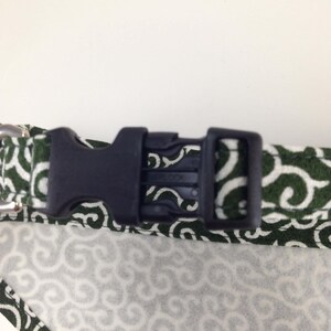 Puede incluir: Primer plano de un collar para perros con una hebilla de pl&aacute;stico negro. El collar presenta una tela blanca con un patr&oacute;n de remolino verde. Los bordes est&aacute;n ribeteados con una tela verde con un patr&oacute;n de remolino blanco.