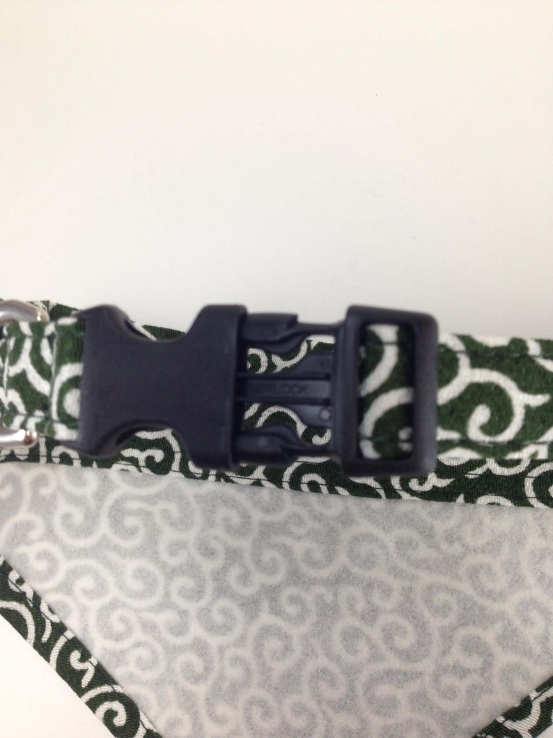 Puede incluir: Primer plano de un collar para perros con una hebilla de pl&aacute;stico negro. El collar presenta una tela blanca con un patr&oacute;n de remolino verde. Los bordes est&aacute;n ribeteados con una tela verde con un patr&oacute;n de remolino blanco.