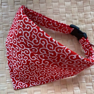 Puede incluir: Collar para mascotas con estampado rojo y blanco con hebilla de pl&aacute;stico negro y anilla met&aacute;lica plateada. El collar presenta un dise&ntilde;o de remolino repetido. El fondo es una superficie tejida de color marr&oacute;n claro.