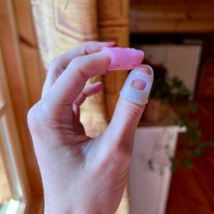 Pode incluir: Dois protetores de dedos, um rosa e um branco, feitos de silicone. Os protetores de dedos têm orifícios para respirabilidade.