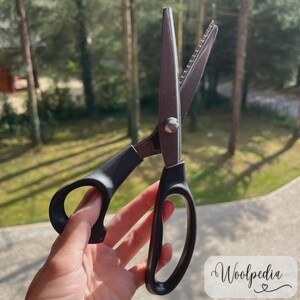 May include: A pair of black-handled shears with a serrated blade, held against a blurred outdoor background. The shears are open, showcasing the sharp blades. The text "Woolpedia" is visible in the lower right corner.