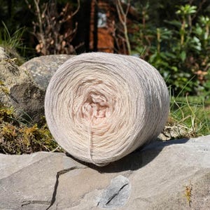 May include: A skein of yarn in a light pink and white color combination. The yarn is wound into a ball shape and is ready for knitting or crocheting.