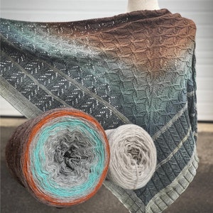 Könnte beinhalten: Ein handgestrickter Schal in Braun-, Grün- und Grautönen mit einem geometrischen Muster. Im Vordergrund sind zwei Garnrollen zu sehen, eine in Braun-, Grau- und Türkistönen und die andere in Hellgrau.