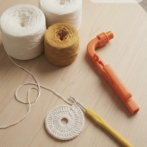 May include: A craft scene with white and mustard yellow yarn skeins, a crochet hook, and an orange yarn cutter. A partially completed white crochet circle is also visible. The image includes the text "Woolpedia".