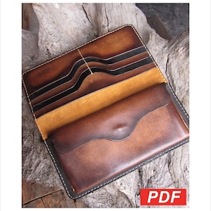 May include: Open, brown leather wallet with multiple card slots and a bill compartment. The wallet has a contrasting white stitch and a flap closure. The interior is a lighter tan color. The wallet is on a wooden surface.