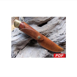 May include: A handcrafted knife with a wooden handle and a brass bolster, encased in a brown leather sheath. The sheath is secured with a brass button closure. The knife is displayed on a weathered wood surface.