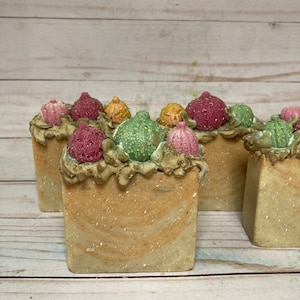 May include: Four bars of handmade soap with a swirl design. Each bar is topped with a variety of colorful, glittery ornaments.