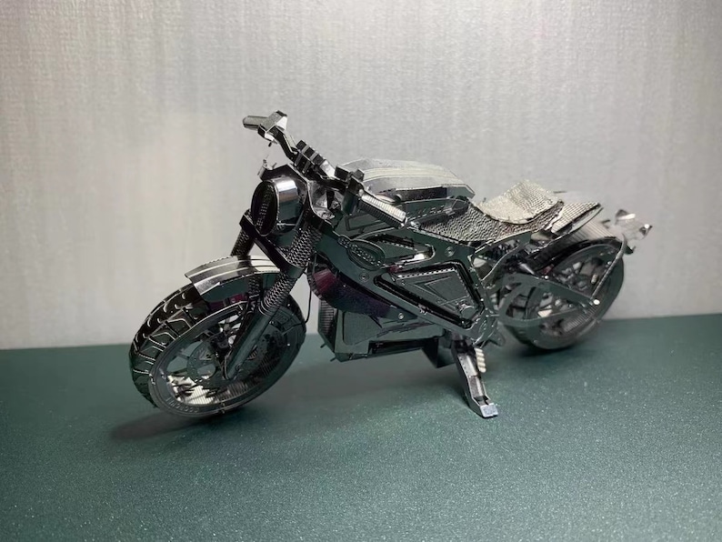 May include: A silver metal model motorcycle with a black seat and wheels. The motorcycle is detailed with a chrome finish and has a kickstand.