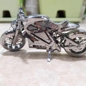 May include: A silver metal model of a motorcycle with a detailed design. The motorcycle has two wheels, a seat, and a handlebar.
