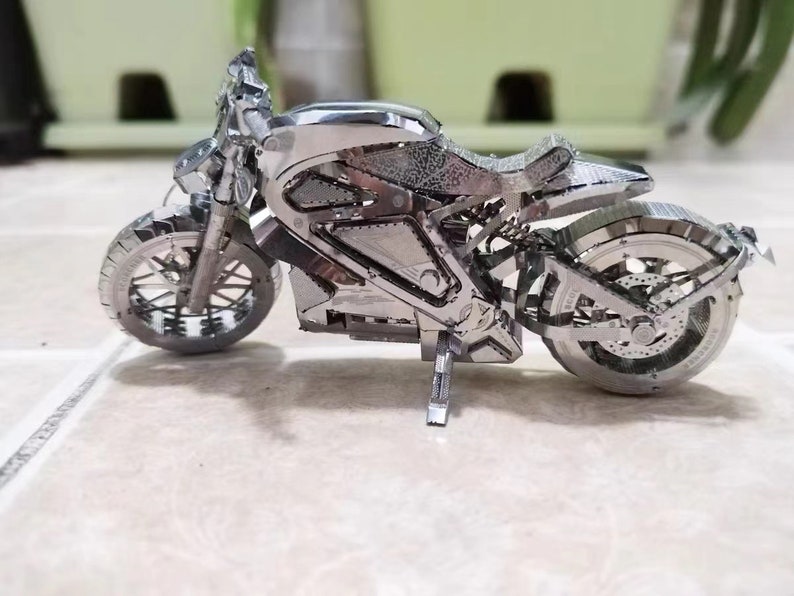 May include: A silver metal model of a motorcycle with a detailed design. The motorcycle has two wheels, a seat, and a handlebar.