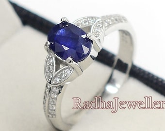 Può includere: Un anello d'argento con una grande pietra preziosa ovale blu scuro come elemento centrale. L'anello presenta pietre preziose più piccole e trasparenti e dettagli decorativi a forma di foglia sulla fascia. L'anello è esposto in un cofanetto nero.