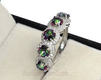 Può includere: Un anello d'argento con cinque pietre preziose iridescenti, ciascuna circondata da un alone di piccole pietre trasparenti. L'anello è presentato in un cofanetto nero con interno bianco. Le pietre mostrano colori come verde, viola e blu.