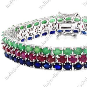 May include: A multi-strand bracelet featuring rows of green, red, and blue gemstones set in a silver metal. The gemstones are oval-cut and arranged in a repeating pattern. The bracelet has a clasp closure.