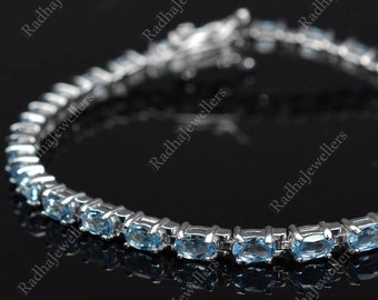 May include: A silver bracelet featuring a series of oval, light blue gemstones. The gemstones are set in a row, connected by a silver chain. The bracelet is displayed against a dark background, highlighting the sparkle of the gems.
