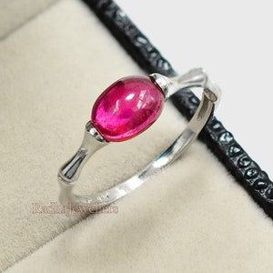 May include: A silver ring with a pink oval gemstone. The ring is in a black velvet ring box.