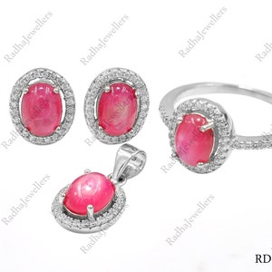 Könnte beinhalten: Ein Schmuckset bestehend aus einem Ring, einem Anhänger und einem Paar Ohrsteckern. Jedes Stück zeigt einen ovalen, im Cabochon-Schliff geschliffenen rosa Edelstein, umgeben von einem Kranz aus kleinen weißen Steinen in einer silberfarbenen Fassung.