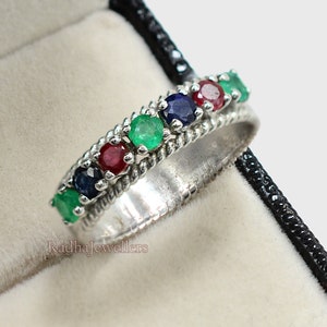 Peut inclure: Une bague en argent avec un design de corde torsadée et une rangée de pierres précieuses émeraude, rubis et saphir.