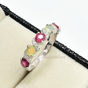 Peut inclure: Une bague en argent avec une rangée de pierres précieuses rouges et blanches alternées, et une opale blanche plus grande au centre.