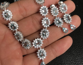 Può includere: Un set di collana, bracciale e orecchini in argento con pietre preziose ovali blu chiaro e pietre chiare di contorno. La collana ha un pendente a goccia. Gli orecchini sono a goccia.