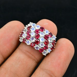 Könnte beinhalten: Ein silberner Ring mit einem mehrreihigen Design aus abwechselnd roten und weißen Edelsteinen. Der Ring ist mit runden, facettierten Steinen besetzt.