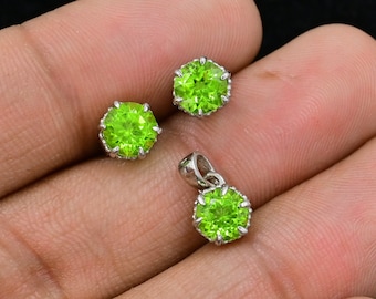 May include: A set of green peridot gemstone jewelry, including a pendant and a pair of earrings. The jewelry is made of sterling silver and features a round, faceted peridot stone in each piece.