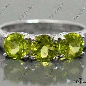 May include: A silver ring with three green peridot gemstones. The ring is set with three round stones in a row.