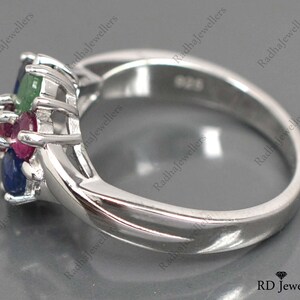 May include: A silver ring featuring a cluster of blue, green, and red gemstones. The ring is set with a delicate, intricate design.