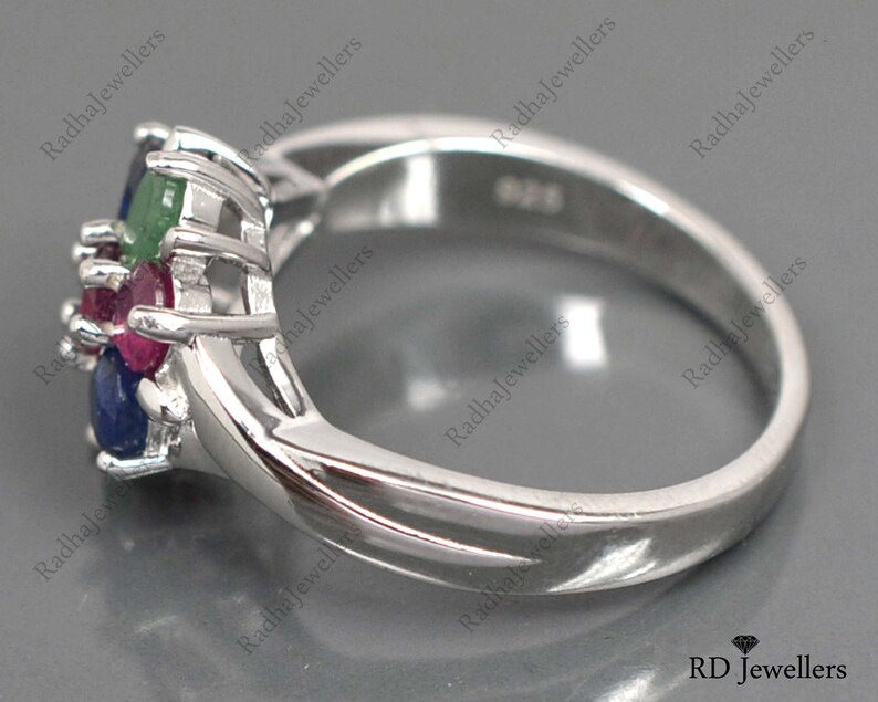 May include: A silver ring featuring a cluster of blue, green, and red gemstones. The ring is set with a delicate, intricate design.