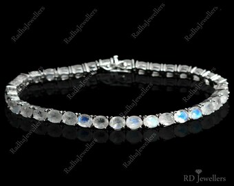 Puede incluir: Un brazalete de plata con una fila de gemas de piedra lunar ovaladas. El brazalete está hecho de plata de ley y tiene un acabado pulido.