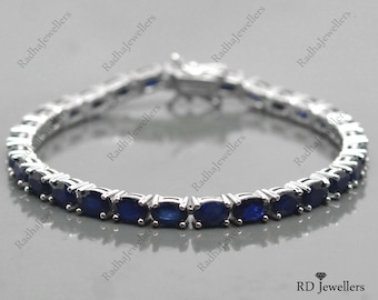 May include: A silver tennis bracelet with a row of oval-shaped blue gemstones.
