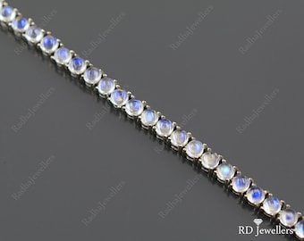 Puede incluir: Un brazalete de plata con una fila de piedras redondas de piedra lunar iridiscente. El brazalete está sobre un fondo gris.