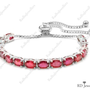 May include: A silver-toned adjustable bolo bracelet featuring a series of oval-cut, vibrant red gemstones set in individual metal prongs. The bracelet includes a sliding mechanism with two small silver spheres at the ends of the box chain links.
