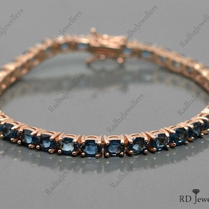May include: A rose gold tennis bracelet with blue topaz stones. The bracelet is made of 14k rose gold and features a classic tennis bracelet design.