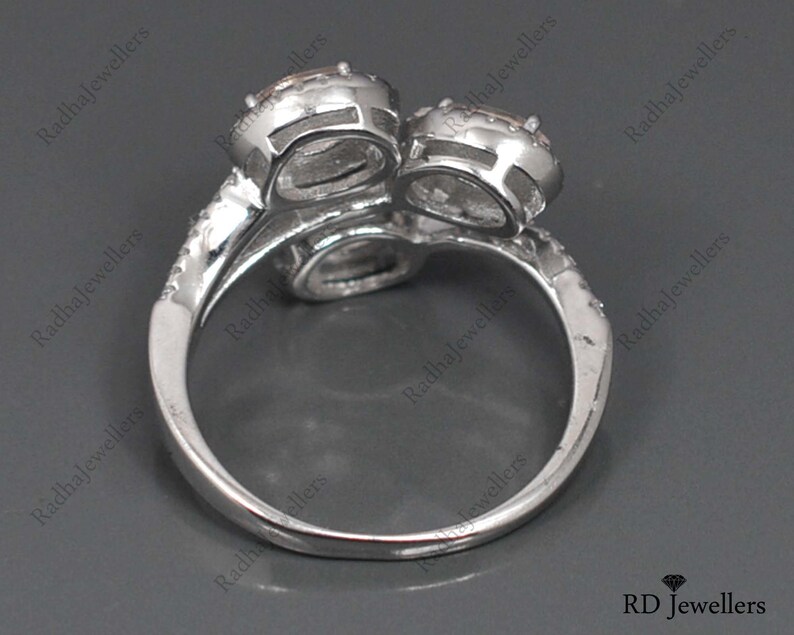 May include: A silver ring with two large, clear stones set in a twisted band. The ring is on a gray background.