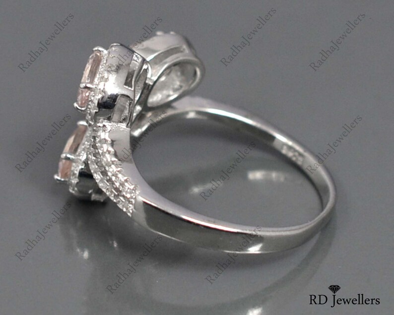 May include: A silver ring with two pink gemstones set in a twisted band. The ring is designed to be worn on the knuckle.