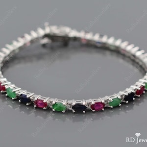 Peut inclure: Un bracelet de tennis en argent avec des pierres précieuses ovales de couleur rouge, verte et bleue alternées. Le bracelet est doté d'une fermeture à fermoir.