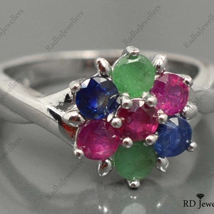 May include: A silver ring featuring a cluster of colourful gemstones. The ring has a flower-shaped design with green, blue, and red stones.