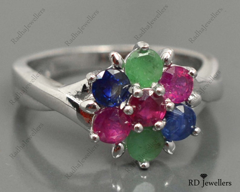 May include: A silver ring featuring a cluster of colourful gemstones. The ring has a flower-shaped design with green, blue, and red stones.