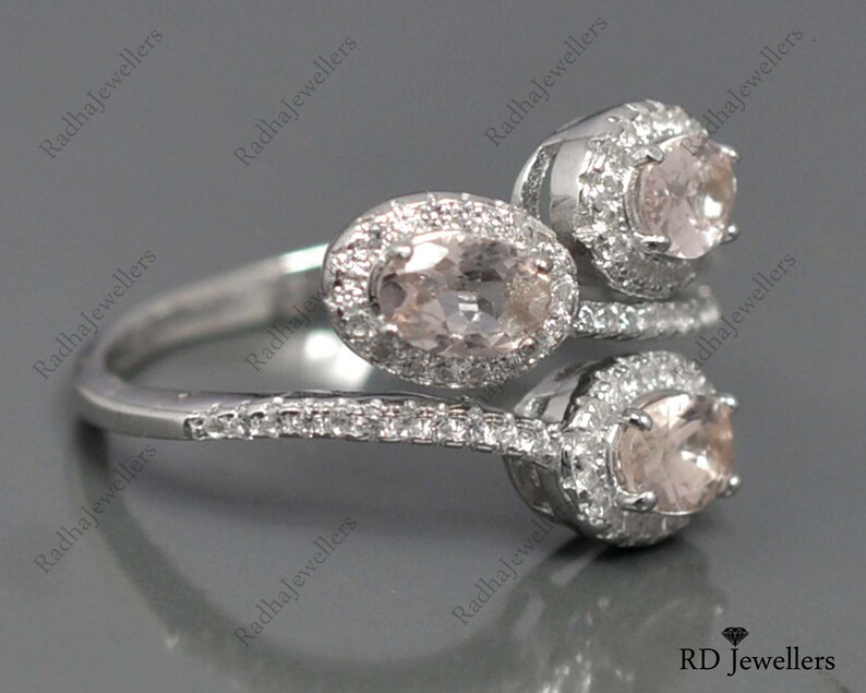 May include: A silver ring with three oval-shaped pink gemstones set in a halo of smaller clear gemstones. The ring has a twisted band.