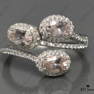 May include: A silver ring with three oval-shaped pink gemstones surrounded by smaller clear gemstones. The ring has a twisted band.
