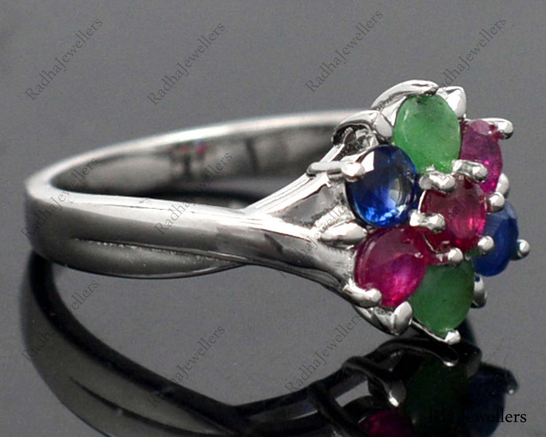 May include: A silver ring featuring a cluster of five oval-shaped gemstones in shades of red, blue, and green. The ring is set in a silver band.